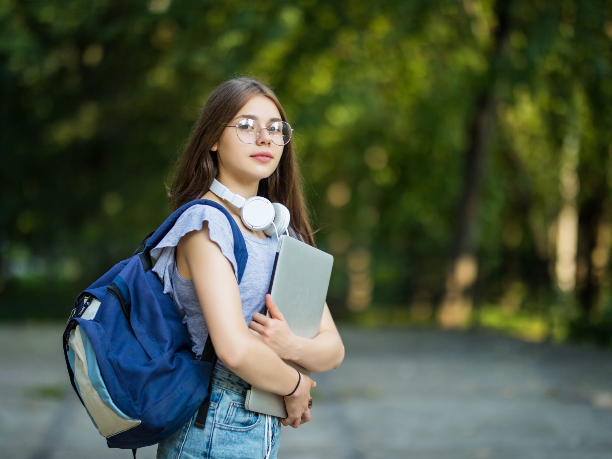 Cheerful attractive woman with backpack and notebooks standing and smiling in park